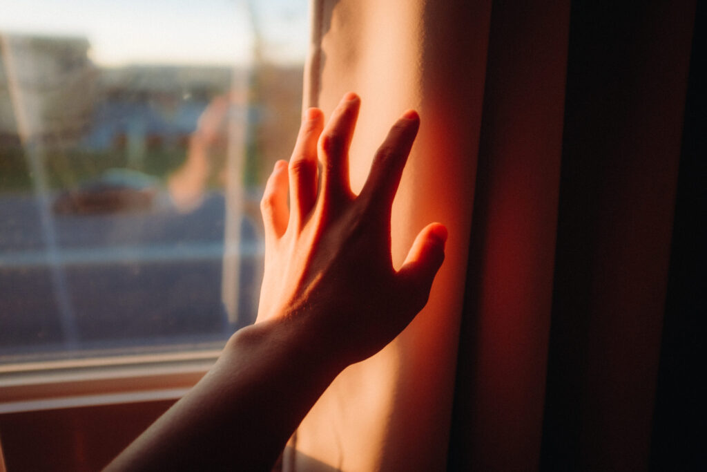 hand reaching out towards a window in themorning light Photo by Jordon Hon